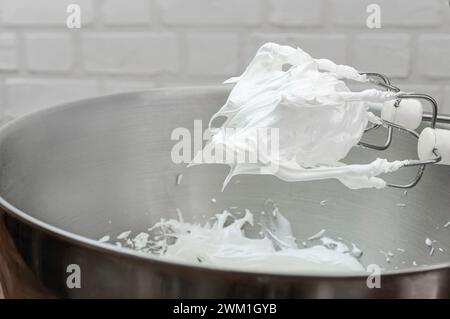 Verschlagene Eiweiß mit Zucker für Meringue in einer Schüssel mit einem elektrischen Handquirl. Kochprozess mit Küchenutensilien. Stockfoto