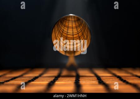 Aufnahme des konvexen Teils eines hängenden Silberlöffels, der das lineare Design der darunter liegenden Ebene reflektiert, beleuchtet durch einen Lichtstrahl von oben Stockfoto