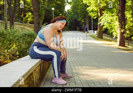 Fette Frau in Sportbekleidung, die im Sommer-Stadtpark sitzt und nach Sportübungen ruht. Stockfoto