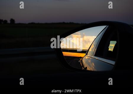 Blick im Außenspiegel eines Autos. Blick vom Inneren des Fahrzeugs. Abendliche Autofahrt auf der Autobahn. Stockfoto