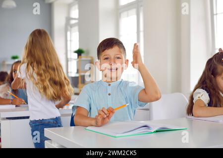 Porträt eines kleinen aktiven Schuljungen, der im Unterricht seine Hand hebt, um Fragen oder Antworten zu stellen. Stockfoto