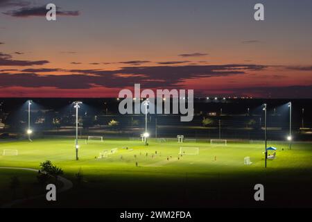 Blick aus der Vogelperspektive auf den öffentlichen Sportpark mit Menschen, die bei Sonnenuntergang im Grasstadion spielen. Aktives Lebenskonzept. Stockfoto