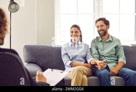 Glückliches, lächelndes junges Paar, das auf der Couch im Büro des Ratgebers sitzt, Ratschläge hört und lächelt. Stockfoto