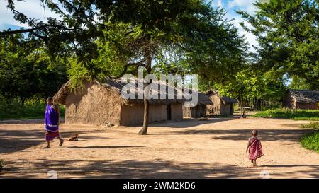 Ein junges Maasai-Mädchen und eine Maasai-Frau laufen in der Nähe von Häusern in ihrem Dorf Mikumi in Tansania. Stockfoto