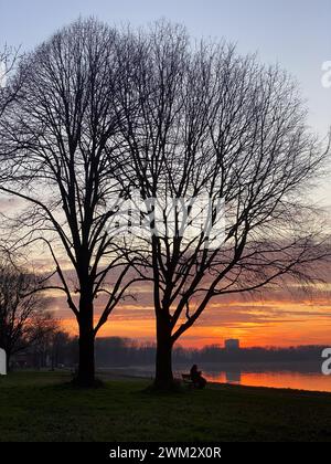 Fluss Po und lebhafter Sonnenuntergang im Hintergrund. Der Himmel ist in Orangentönen gemalt und reflektiert das plätschernde Wasser. San Nazzaro, PC, Italien Stockfoto