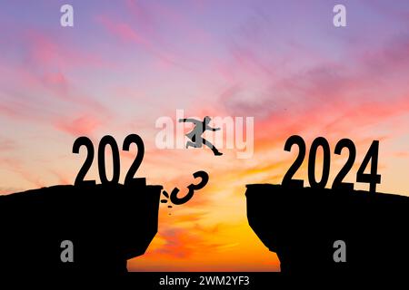 Mann springt auf Klippe 2024 über den Abgrund mit Steinen bei erstaunlichem Sonnenuntergang. Neujahrskonzept. 2023 fällt in den Abgrund. Willkommen 2024. Stockfoto