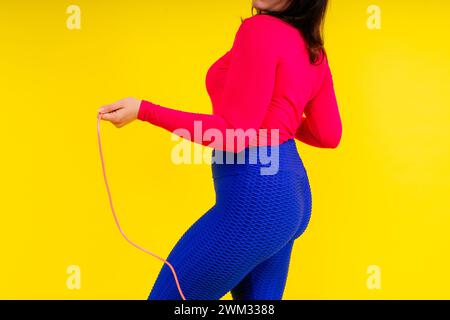 Hübsch lächelnde, pralle Frau in sportlichem Oberteil und Leggings, die ein Springseil in den Händen hält Stockfoto