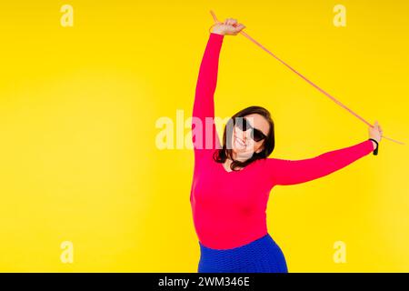 Hübsch lächelnde, pralle Frau in sportlichem Oberteil und Leggings, die ein Springseil in den Händen hält Stockfoto