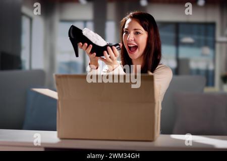 Lächelnde junge Frau sitzt auf einem Sofa Auspacken empfangene Paket Stockfoto