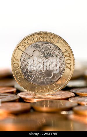 Studio-Aufnahme einer zwei-Pfund-Münze in Sterling-Währung, die aufrecht auf dem Tisch steht, mit unscharfen Münzen im Vordergrund vor weißem Hintergrund Stockfoto