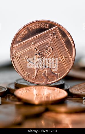 Studio-Aufnahme eines zwei-Pence-Stücks in Sterling-Währung, der aufrecht auf dem Tisch steht, mit unscharfen Münzen im Vordergrund vor weißem Hintergrund Stockfoto