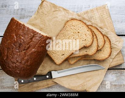 Das Konzept traditioneller Backmethoden für gesäuertes Brot. Geschnittenes Vollkornbrot auf dunklem rustikalem Holzbrett aus nächster Nähe. Traditionelles Sauerteigbrot Schnitt i Stockfoto