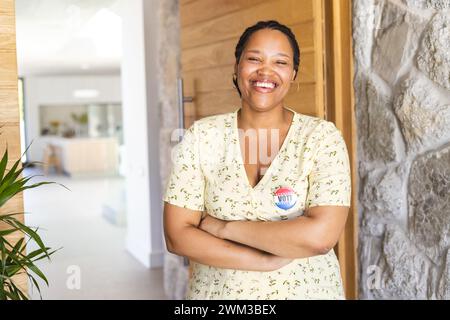 Junge birassische Frau steht selbstbewusst zu Hause mit einem Abstimmungsabzeichen und Kopierraum Stockfoto