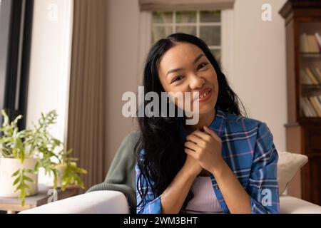 Eine junge Frau mit birassischer Rasse lächelt bei Videogesprächen herzlich, sitzt drinnen Stockfoto