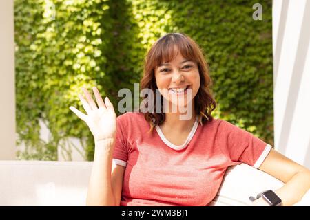 Die junge Frau winkt fröhlich bei Videogesprächen, sitzt draußen Stockfoto