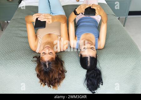 Zwei junge Frauen liegen auf einem Bett und benutzen Smartphones Stockfoto