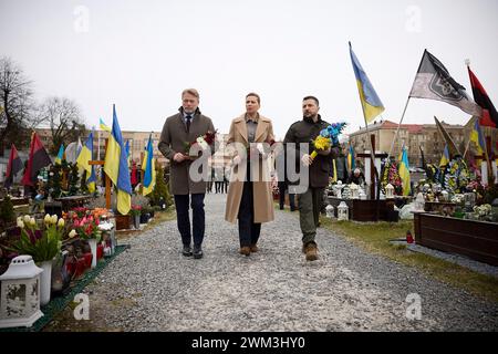 Lviv, Ukraine. Februar 2024. Der ukrainische Präsident Wolodymyr Zelenskyj, rechts, geht mit dem dänischen Premierminister Mette Frederiksen, dem Zentrum, und seinem Ehemann Bo Tengberg, während sie gefallenen Soldaten auf dem Marsfeld auf dem Lytschakiw-Friedhof am 23. Februar 2024 in Lemberg, Ukraine, ihren Respekt zollen. Quelle: Pool Photo/Ukrainische Präsidentenpresse/Alamy Live News Stockfoto