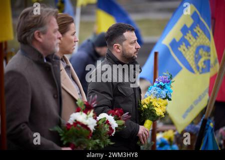 Lviv, Ukraine. Februar 2024. Der ukrainische Präsident Wolodymyr Zelenskyj, rechts, geht mit dem dänischen Premierminister Mette Frederiksen, dem Zentrum, und seinem Ehemann Bo Tengberg, während sie gefallenen Soldaten auf dem Marsfeld auf dem Lytschakiw-Friedhof am 23. Februar 2024 in Lemberg, Ukraine, ihren Respekt zollen. Quelle: Pool Photo/Ukrainische Präsidentenpresse/Alamy Live News Stockfoto