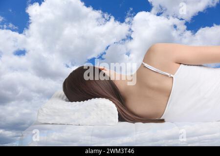 Frau, die auf orthopädischem Kissen vor blauem Himmel schläft Stockfoto