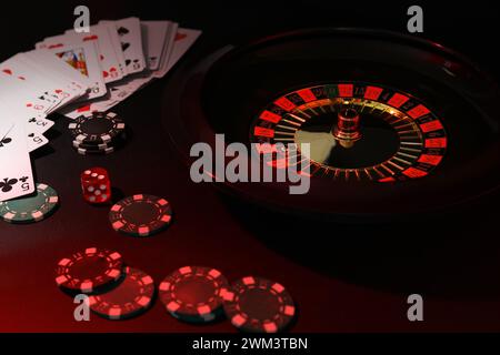 Roulette-Rad mit Ball, Chips, Würfeln und Spielkarten auf dunklem Tisch, Nahaufnahme. Casino-Spiel Stockfoto