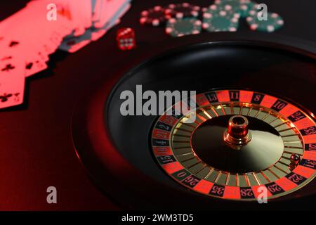 Roulette-Rad mit Ball, Chips, Würfeln und Spielkarten auf dunklem Tisch, Nahaufnahme. Casino-Spiel Stockfoto