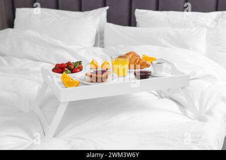 Weißes Tablett mit leckerem Frühstück im Bett Stockfoto