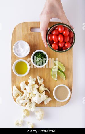 Zutaten für gebratene Blumenkohltomaten und Hummus-Salat auf weißem Hintergrund Stockfoto