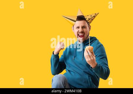 Glücklicher lustiger Mann mit Geburtstagskuchen auf gelbem Hintergrund Stockfoto