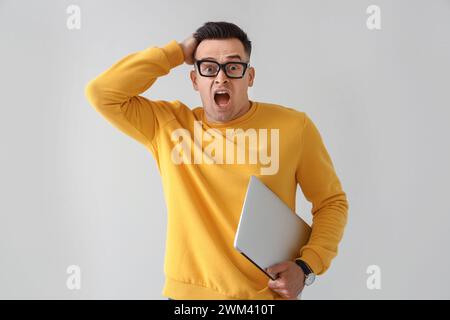 Schockierter junger Mann mit Laptop auf hellem Hintergrund. Terminkonzept Stockfoto