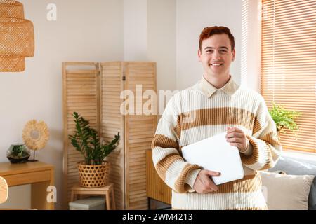 Rothaariger junger glücklicher Mann mit Laptop zu Hause Stockfoto