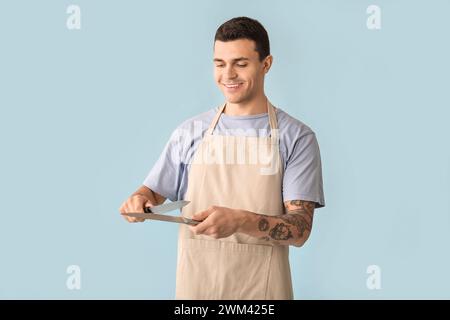 Hübscher, glücklicher männlicher Koch mit Messern auf blauem Hintergrund Stockfoto