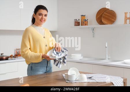 Schöne junge glückliche Frau, die sauberes Geschirr in der Küche abwischt Stockfoto