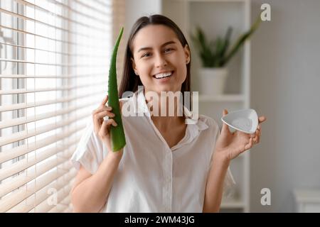 Schöne junge Frau mit einem Teller Aloe Vera Gel in der Nähe des Fensters zu Hause Stockfoto