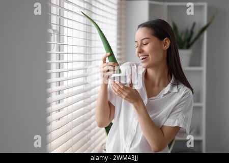 Schöne junge Frau mit einem Teller Aloe Vera Gel in der Nähe des Fensters zu Hause Stockfoto