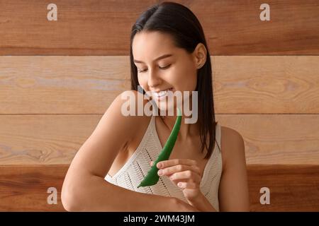 Schöne junge glückliche Frau mit Aloe Vera Blatt auf braunem hölzernem Hintergrund Stockfoto