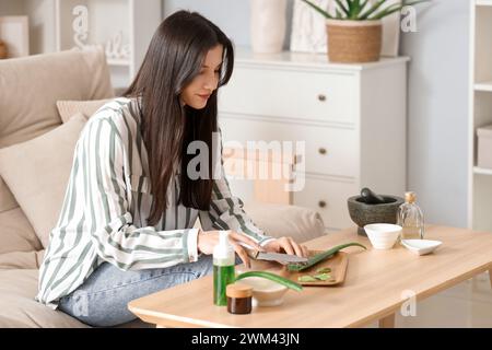 Schöne junge Frau, die Aloe Vera im Wohnzimmer schneidet Stockfoto