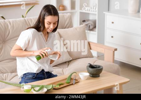 Schöne junge glückliche Frau, die Aloe Vera Gel im Wohnzimmer macht Stockfoto