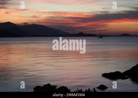 Während die Sonne sich verabschiedet und den Himmel in feurigen Orangetönen malt, gleitet ein einsames Boot sanft über den Horizont, eine Silhouette gegen den Atem der Natur Stockfoto