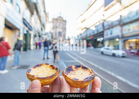 Schleppen Sie Hand mit Portugals traditionellem süßem Dessert Pastel de Nata Eierpudding Torte mit Straße in Porto, Portugal Stockfoto