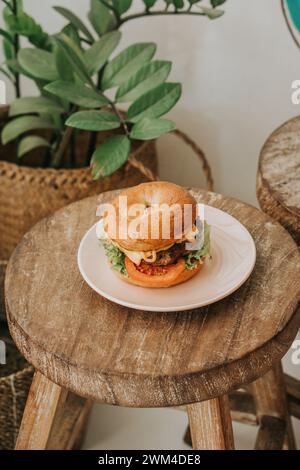 Blick von oben auf einen Double Cheeseburger, der hoch gestapelt ist, Käse tropft, auf einem Holztisch sitzt und dahinter sind Kräuter Stockfoto