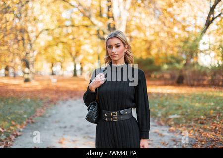 Mode Herbstfrau in schwarz gestricktem, stilvollem Kleid mit trendiger Ledertasche spaziert durch den goldenen Herbstpark Stockfoto