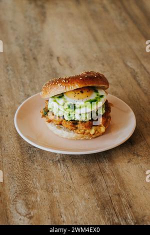 Ein Burger mit Avocado, Spiegelei und geschmolzenem Käse auf einem rosafarbenen Teller Stockfoto