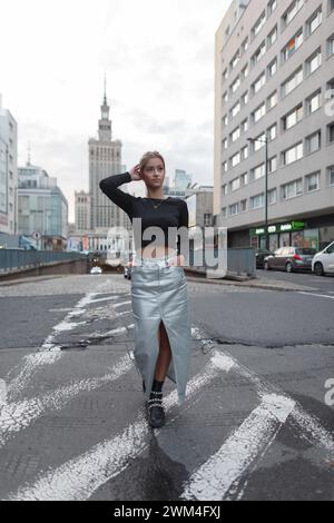 Ein schönes junges, stilvolles Mädchen-Model in Mode-Outfit mit schwarzem Oberteil und silbernem Rock spaziert entlang der Straße in der Stadt. Stockfoto