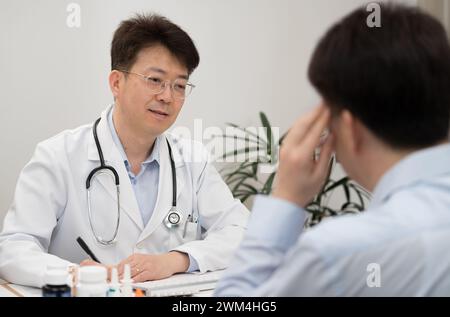 Ein asiatischer Arzt mittleren Alters und ein männlicher Patient, der sich einer Krankenhausberatung unterzieht Stockfoto