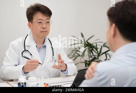 Ein asiatischer Arzt mittleren Alters und ein männlicher Patient, der sich einer Krankenhausberatung unterzieht Stockfoto