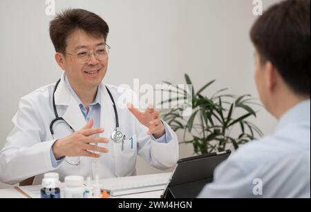 Ein asiatischer Arzt mittleren Alters und ein männlicher Patient, der sich einer Krankenhausberatung unterzieht Stockfoto