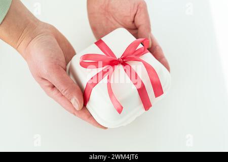 Hände halten eine weiße Box mit einem roten Band und einem bento-Kuchen auf weißem Hintergrund Stockfoto