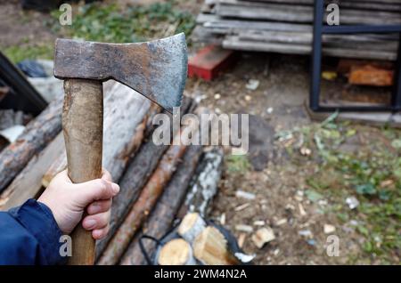 Mann mit Axt. Axt in der Hand. Ein starker Mann hält eine Axt in den Händen vor dem Hintergrund von Feuerholz. Selektiver Fokus, unscharfer Hintergrund Stockfoto