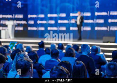 Verschwommenes Bild eines Sprechers auf einer professionellen Konferenz mit einem scharfen Publikum, das aufmerksam zuhört. Stockfoto