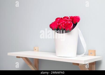 Eine Kiste mit roten Rosen steht auf einem Regal. Strauß von roten Rosen aus Seife. Box mit künstlichen Rosen Stockfoto